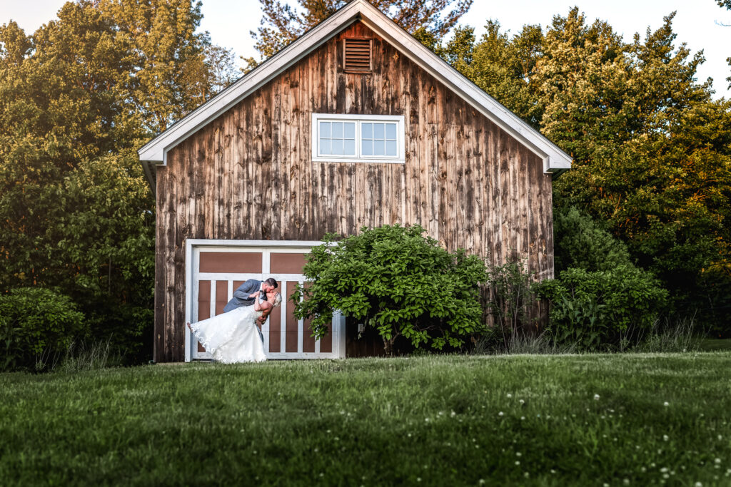 groom dipping bride in front of barn