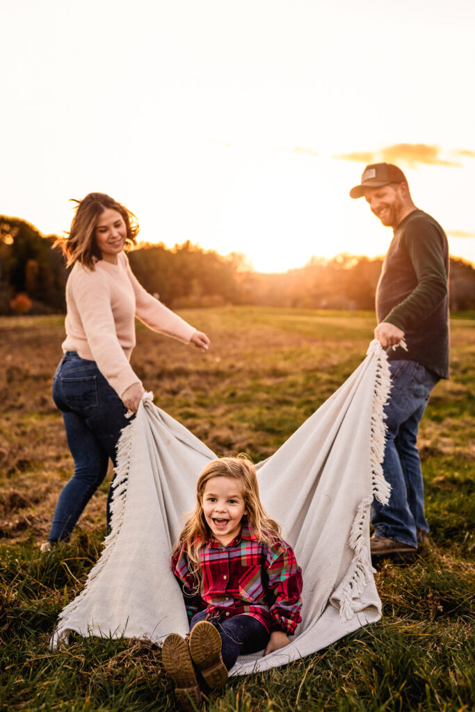 parents pulling girl on blanket at sunset during professional family photo session by lisa smith photography
