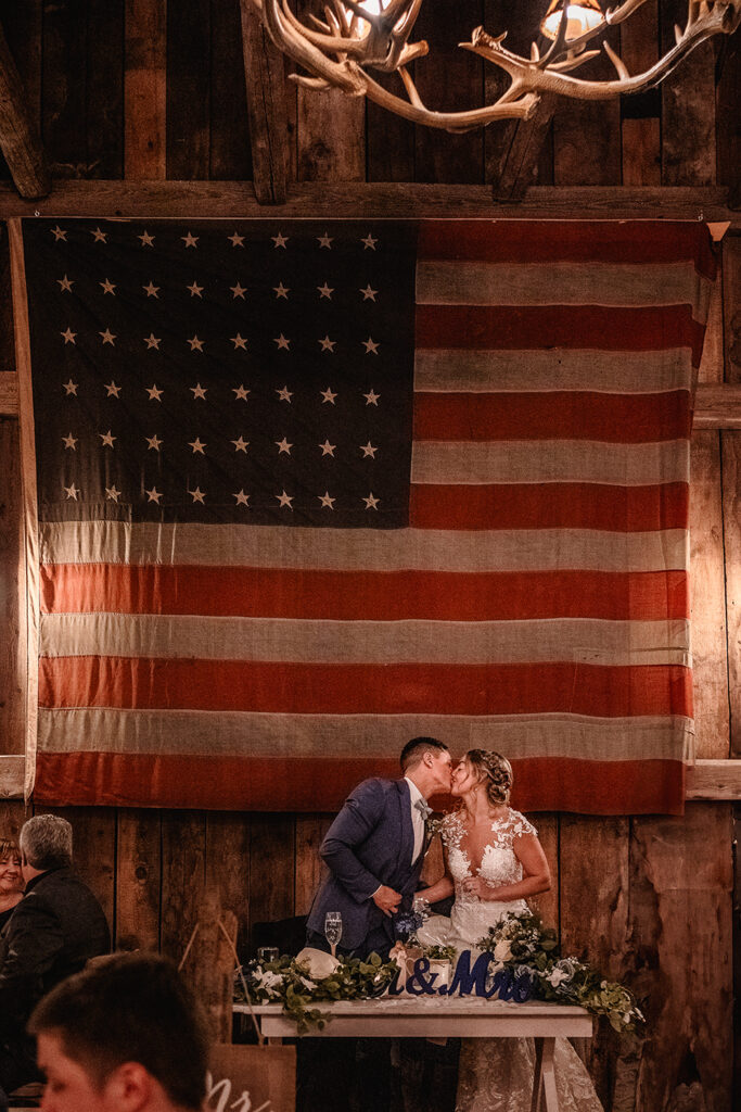 NH Wedding Photographer Bride and Groom Kissing in front of American flag