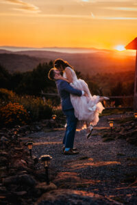 Groom lifting bride for a kiss on path in front of sunset and mountain view at Cobb Hill Estate in Harrisville NH By Lisa Smith Photography