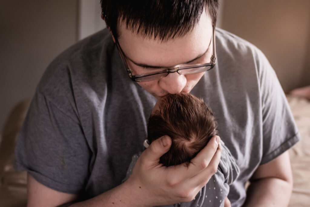 Dad kissing baby on bed during in-home newborn photo session by lisa smith photography