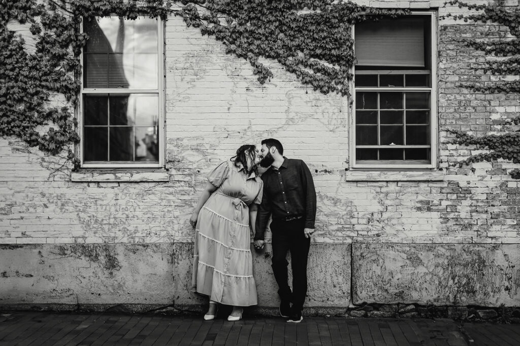 Black and white photog of couple standing together in front of white distressed wall with ivy at Portsmouth NH Engagement Photos by Lisa Smith Photography 
