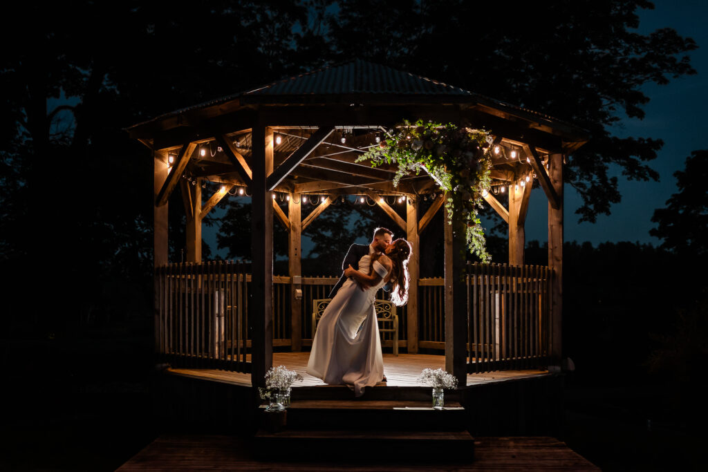 Groom dipping and kissing his bride in gazebo at Josiah's Meetinghouse in Epping in NH Wedding Photography creative night photography