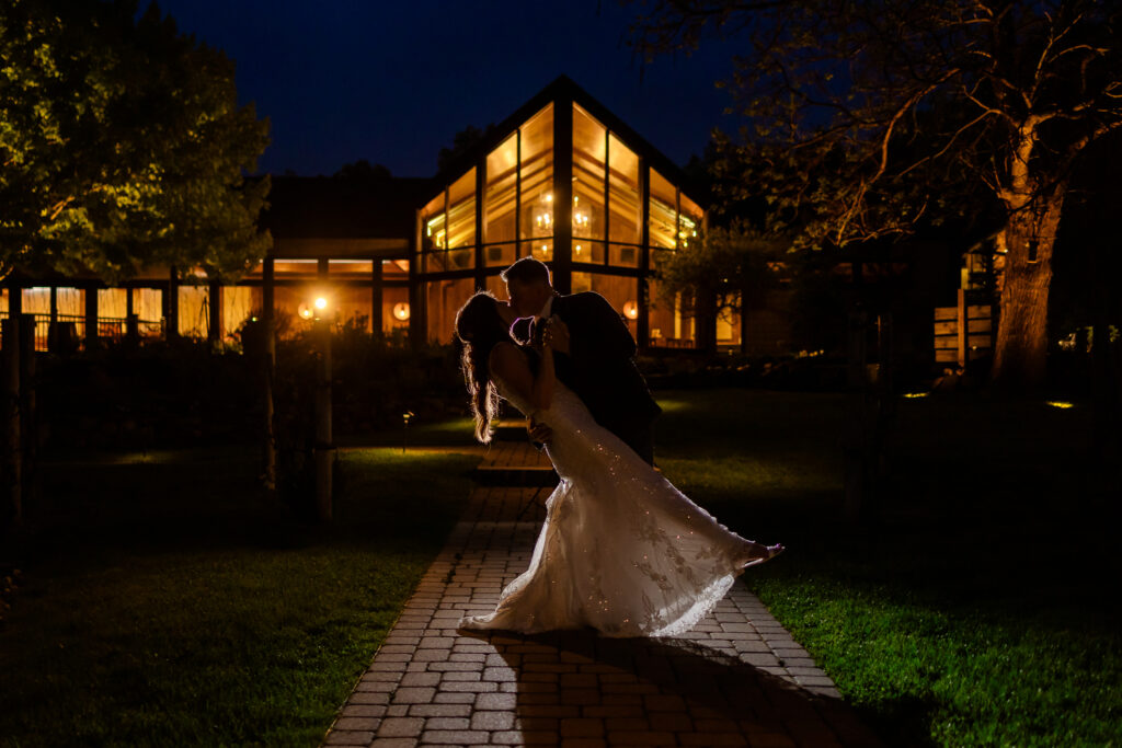 Groom dipping bride with a kiss infront of illuminated Birchwood Vineyard in Derry during NH Wedding Photography creative night photography