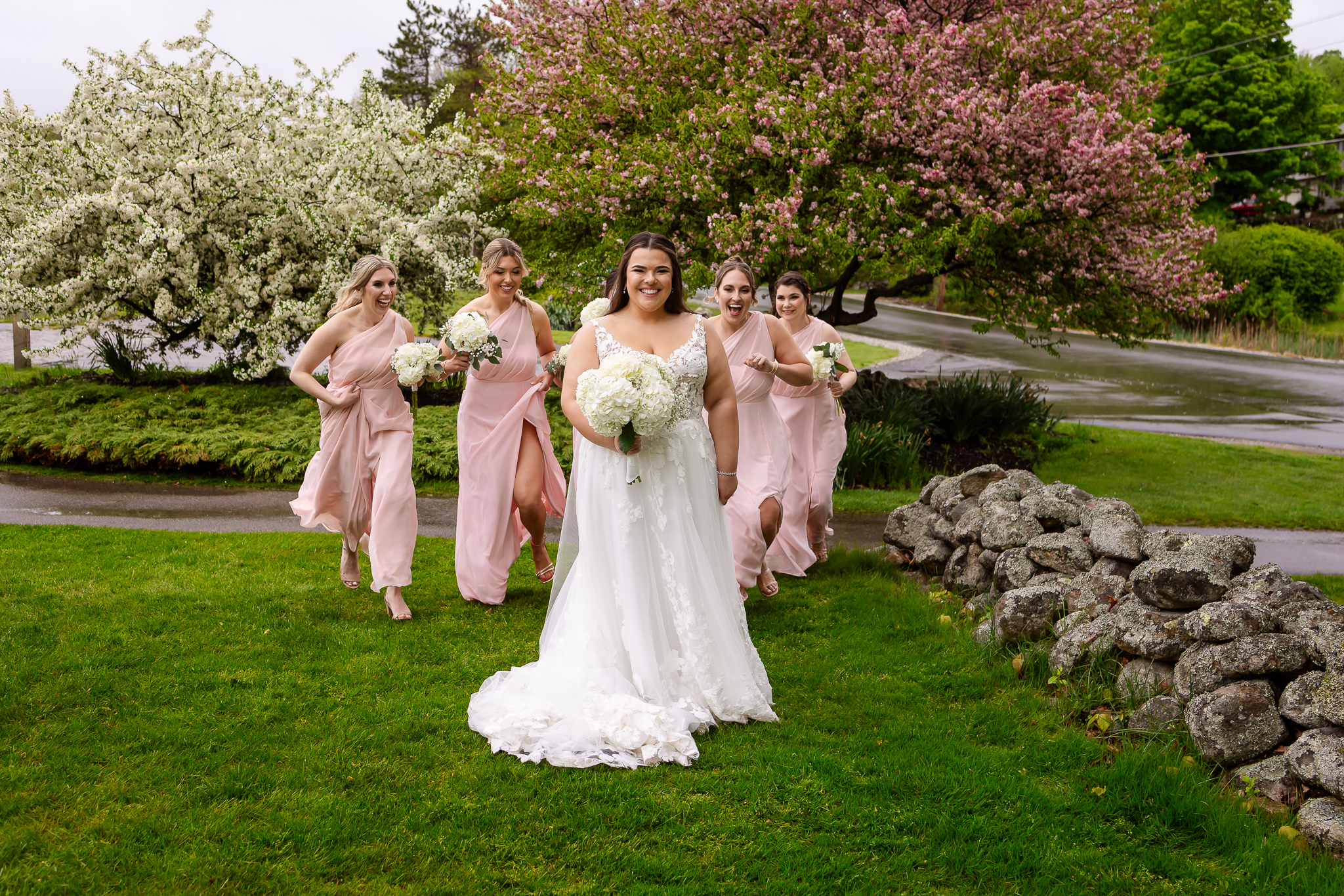 Bridesmaids in blush pink dresses walking behind bride as they sneak up and surprise her.