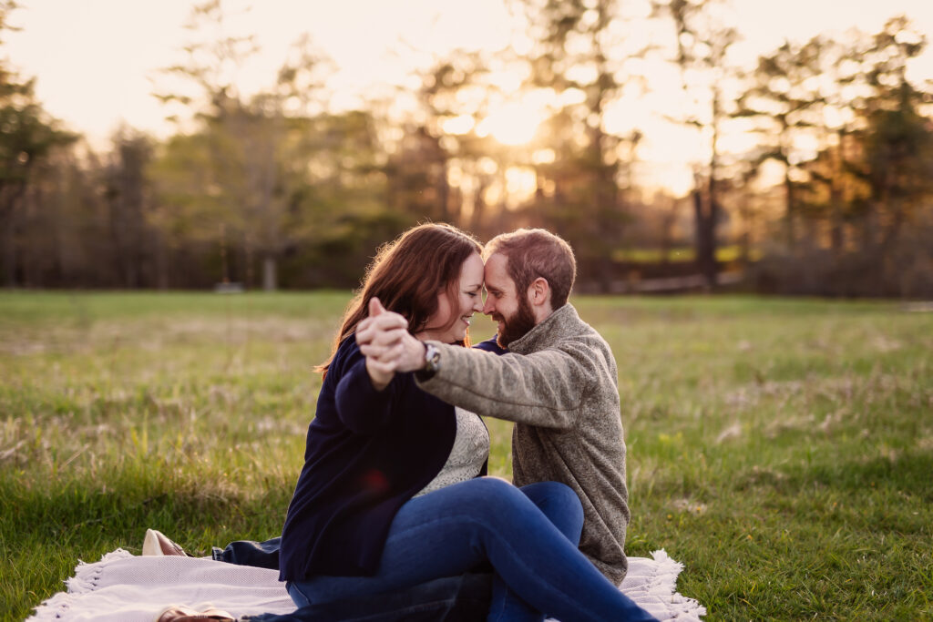 Couple looking into each others eyes while sitting on blanket in field during their engagement photo shoot by NH Wedding Photographer Lisa Smith Photography