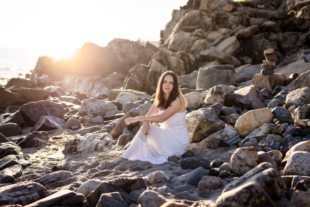 High school senior girl sitting on rocks at sunrise portrait session at york beach ME by NH Senior Photographer Lisa Smith Photography