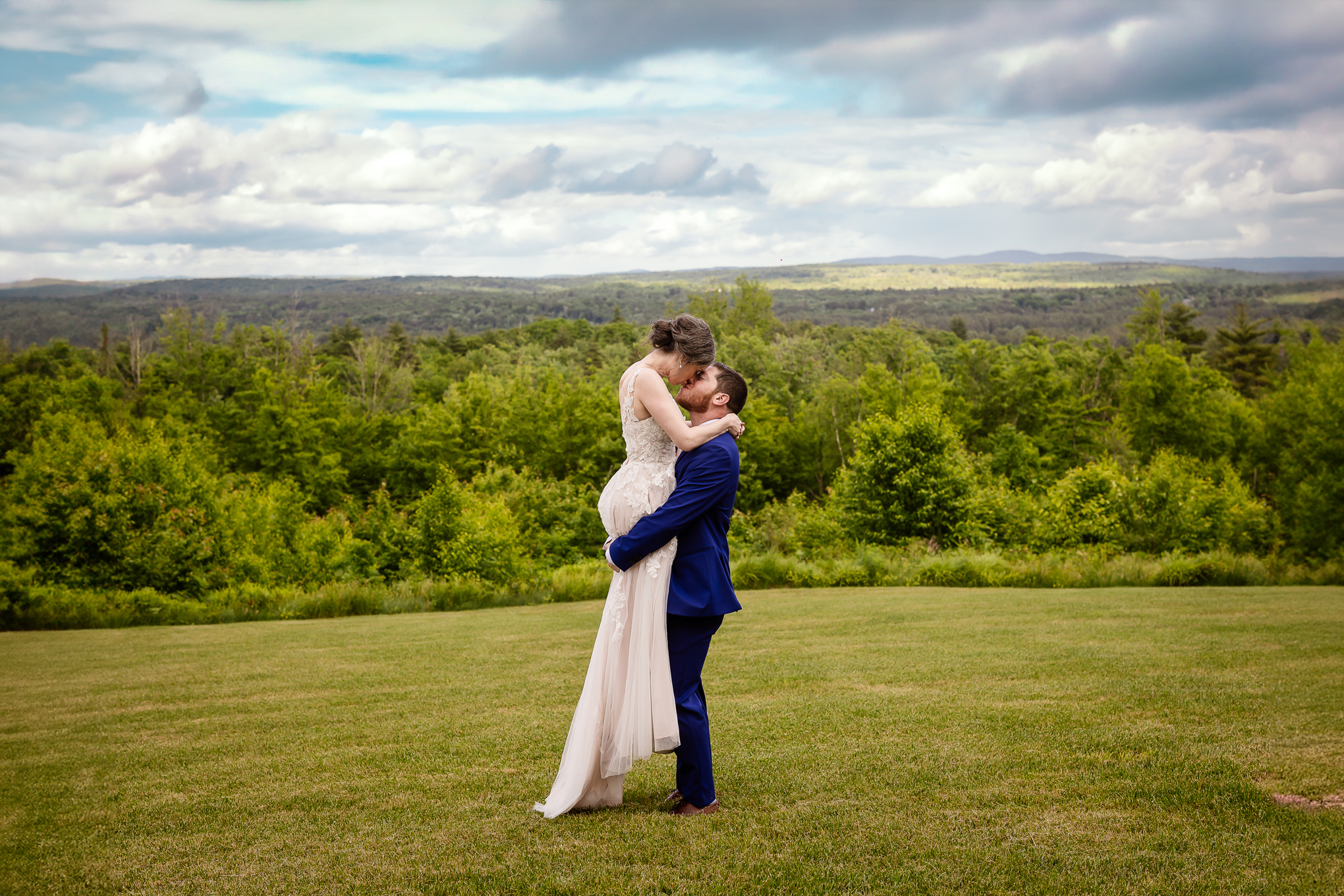 Groom lifting and kissing bride in field with mountain view at Mountain View Stables in Loudon by NH wedding photographer Lisa Smith Photography