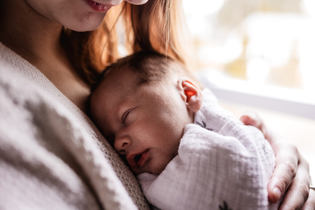 Mom snuggling with newborn baby boy by window during an in home newborn photo session by NH Newborn Photographer Lisa Smith Photography