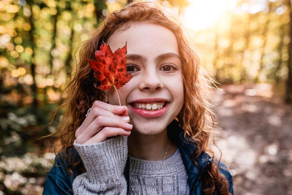 Girl holding a red leaf up to eye during a walk to Beede Falls by NH family photographer Lisa Smith Photography