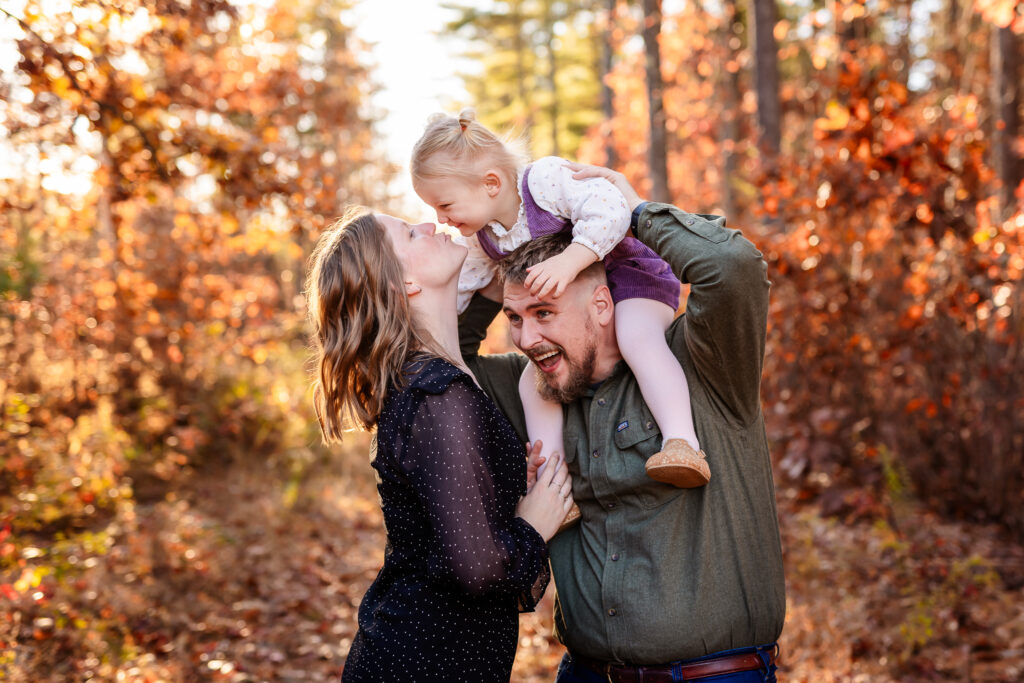 Toddler on dads shoulders and leaning down to kiss mom by NH family photographer Lisa Smith Photography