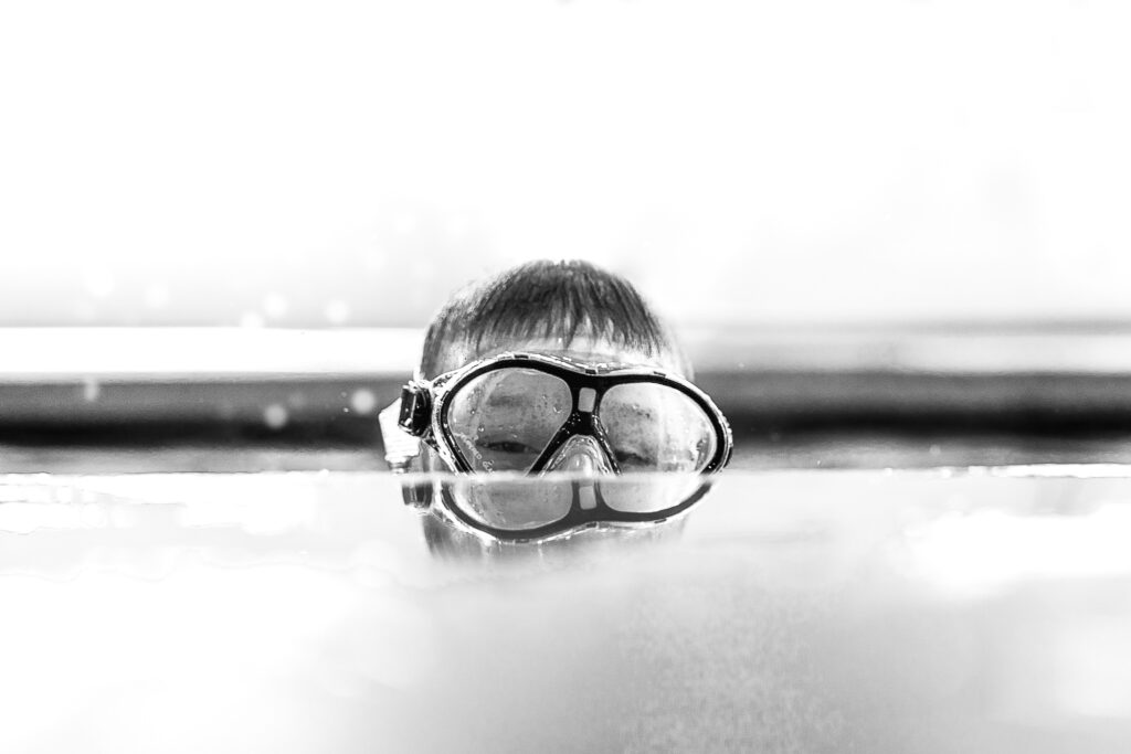 Boy peeking up out of pool with goggles on by NH family photographer Lisa Smith Photography