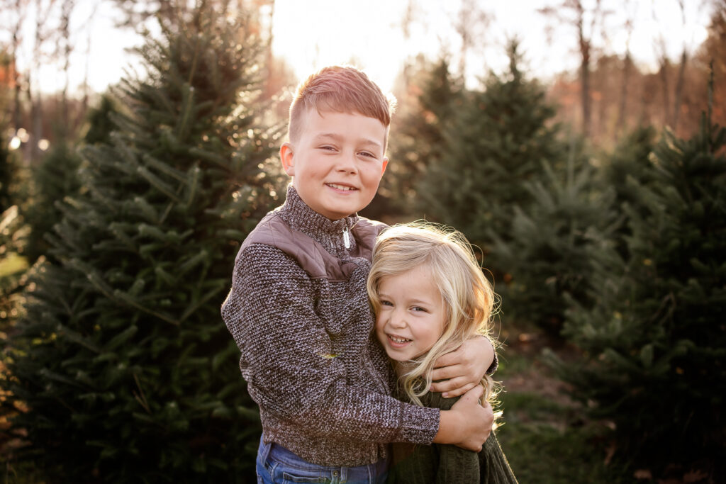 Older brother hugging little sister at a Christmas tree farm by NH family photographer Lisa Smith Photography