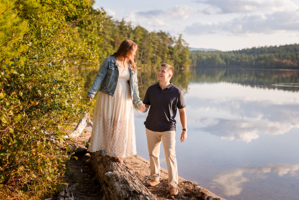 Couple walking along lake in engagement session. Women layered an denim jacket with a long off with dress by NH engagement photographer Lisa Smith Photography