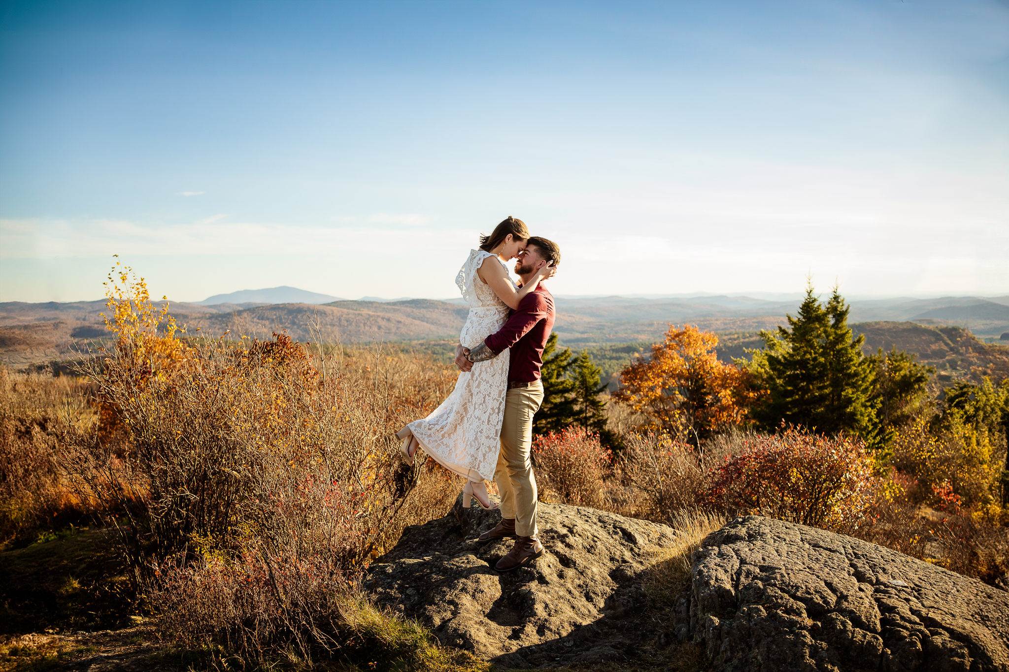 Mountain top engagement session with groom lifting bride and kissing. By NH Wedding Photographer