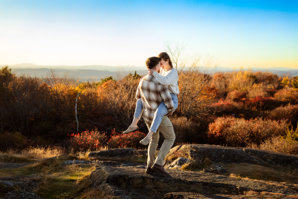 Engagement Mini Photography Session with guy carrying his fiancee over rocks at sunset