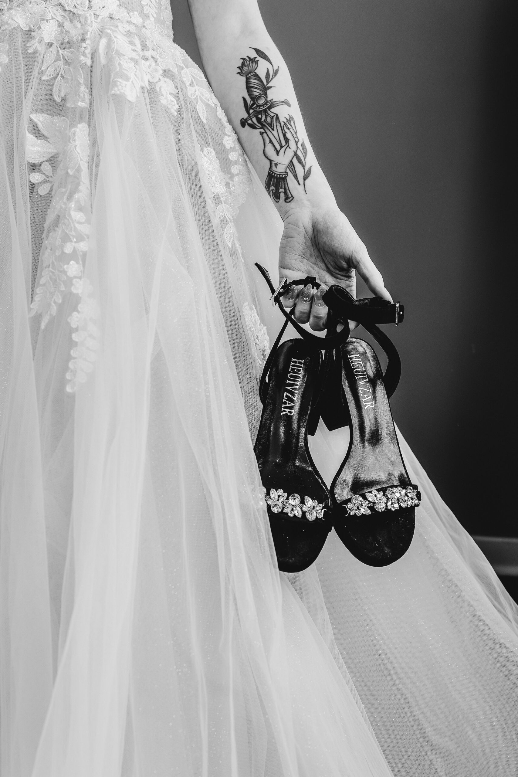 Black and white image of bridal shoes being held next to gown
 