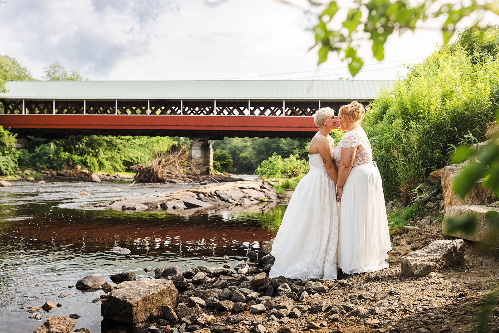 LGBT brides kissing in front of beautiful covered bridge in NH wedding